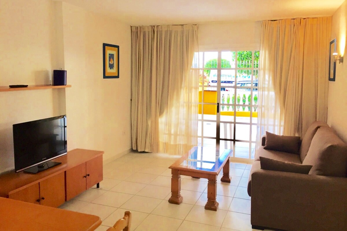 Una sala de estar con televisor, sofá y una mesa de centro de vidrio.