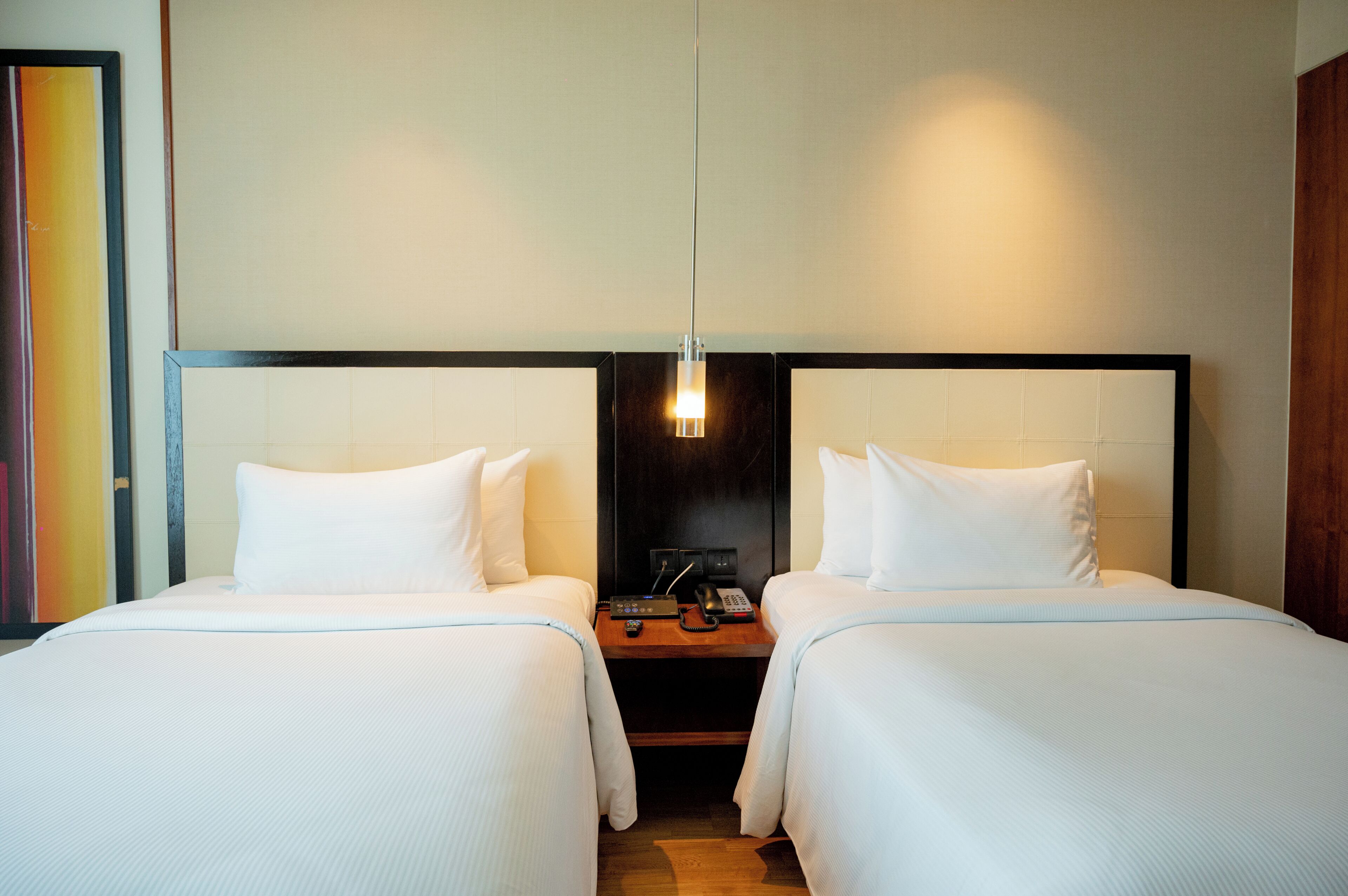 A hotel room with two beds, a nightstand, a lamp, and a painting on the wall.