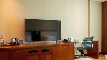 Habitación de hotel con escritorio de madera, televisor de pantalla plana, una silla, cafetera y un cubo de basura.