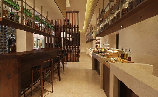 Uma área de bar com prateleiras de garrafas, um balcão com comida e bebidas, e uma área de estar com cadeiras.