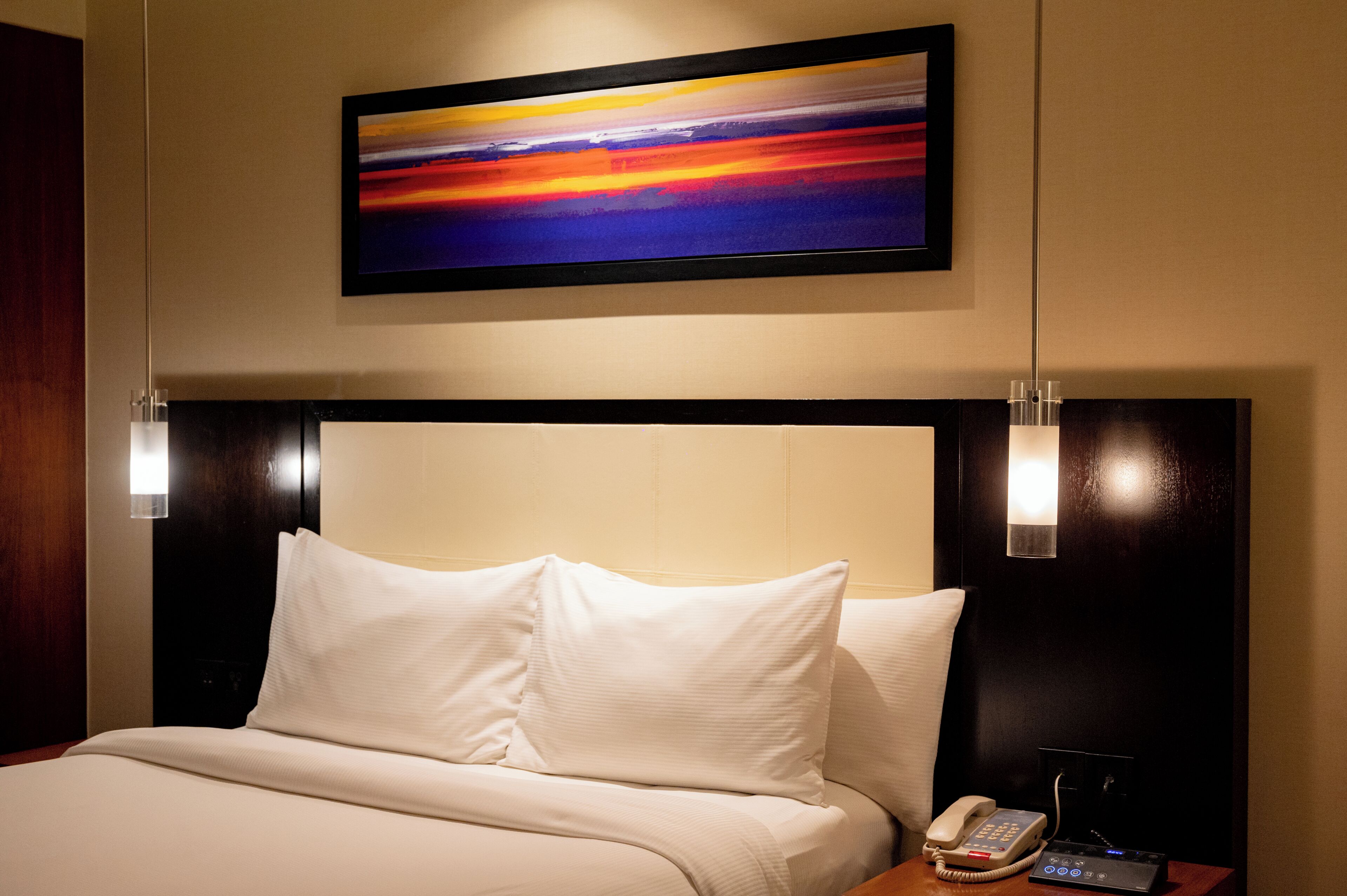 Une chambre d’hôtel avec un lit, un téléphone sur la table de chevet et un tableau au mur.