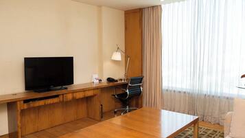 Habitación de hotel con un escritorio de madera, televisor, lámpara, silla y sofá.