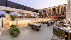 An outdoor dining area with tables and chairs, a bar, and a modern building with geometric patterns. - Doubletree By Hilton Pune - Chinchwad (Pune)