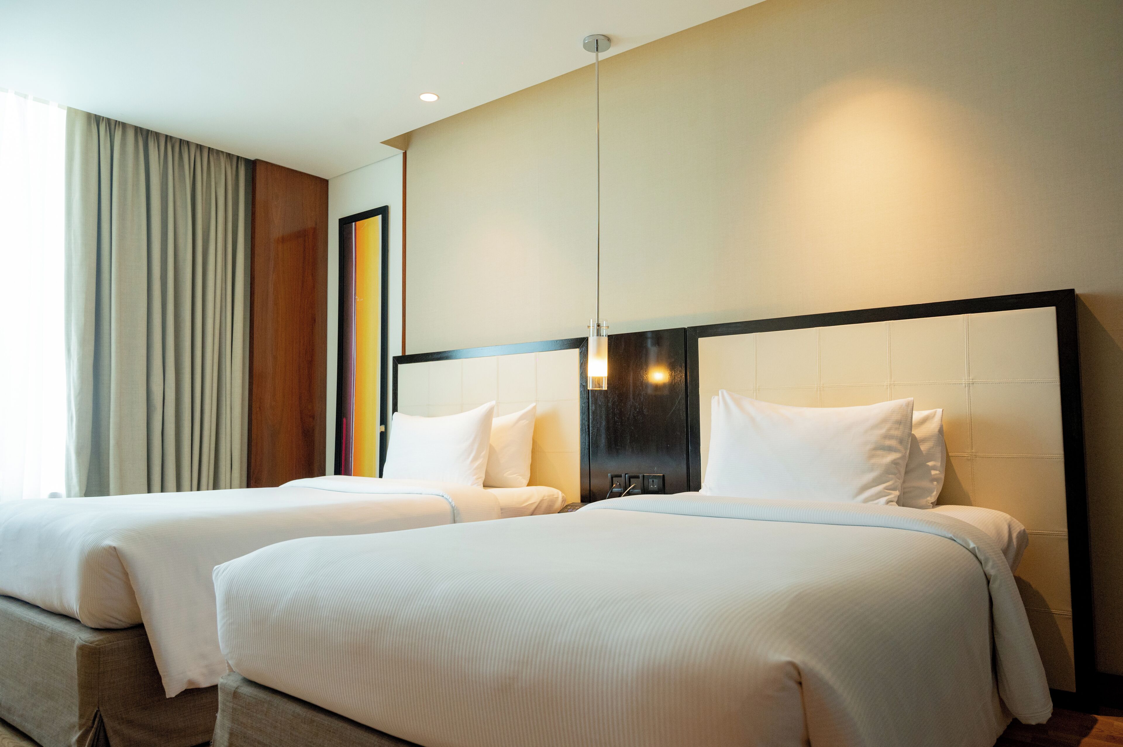 A hotel room with two beds, a large mirror, and a window with curtains.