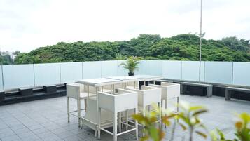 Terraza en la azotea con una mesa y sillas blancas, rodeada por un muro bajo y vista a una colina verde.