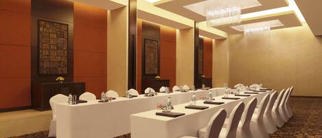 A conference room with long tables, white chairs, and chandeliers.