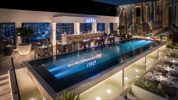 A rooftop pool area with a bar and seating, overlooking a cityscape at night. - Doubletree By Hilton Pune - Chinchwad (Pune)