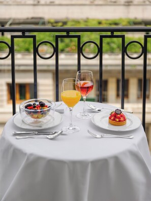 Een tafel met een schaal fruit, twee glazen sap en een dessert op een balkon.