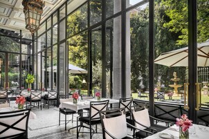 Un'ampia sala da pranzo interna con grandi finestre, tavoli con cornice nera e sedie bianche.