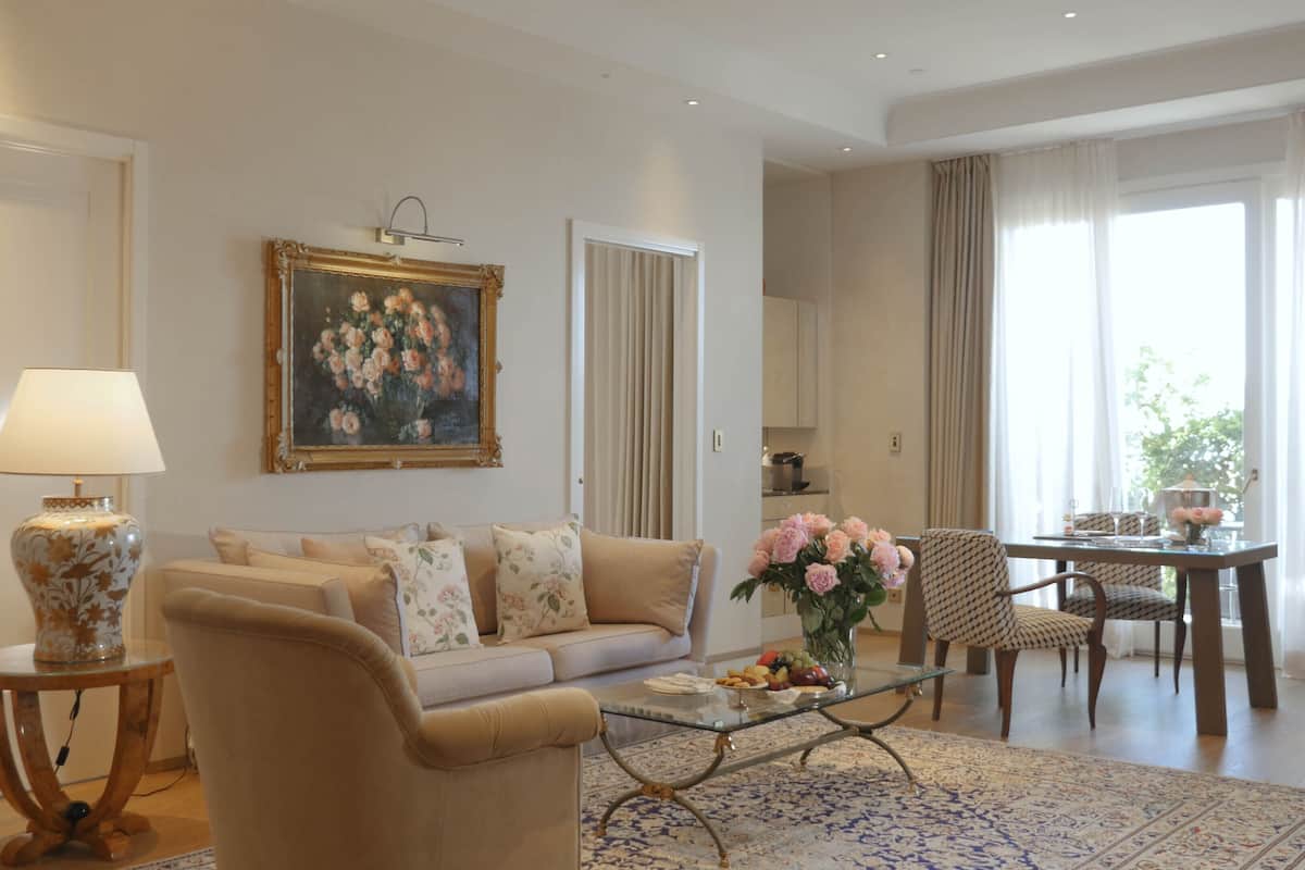 Ein Wohnzimmer mit Sofa, Sesseln, Couchtisch, Lampe, einem Gemälde und einem Essbereich mit Tisch und Stühlen.