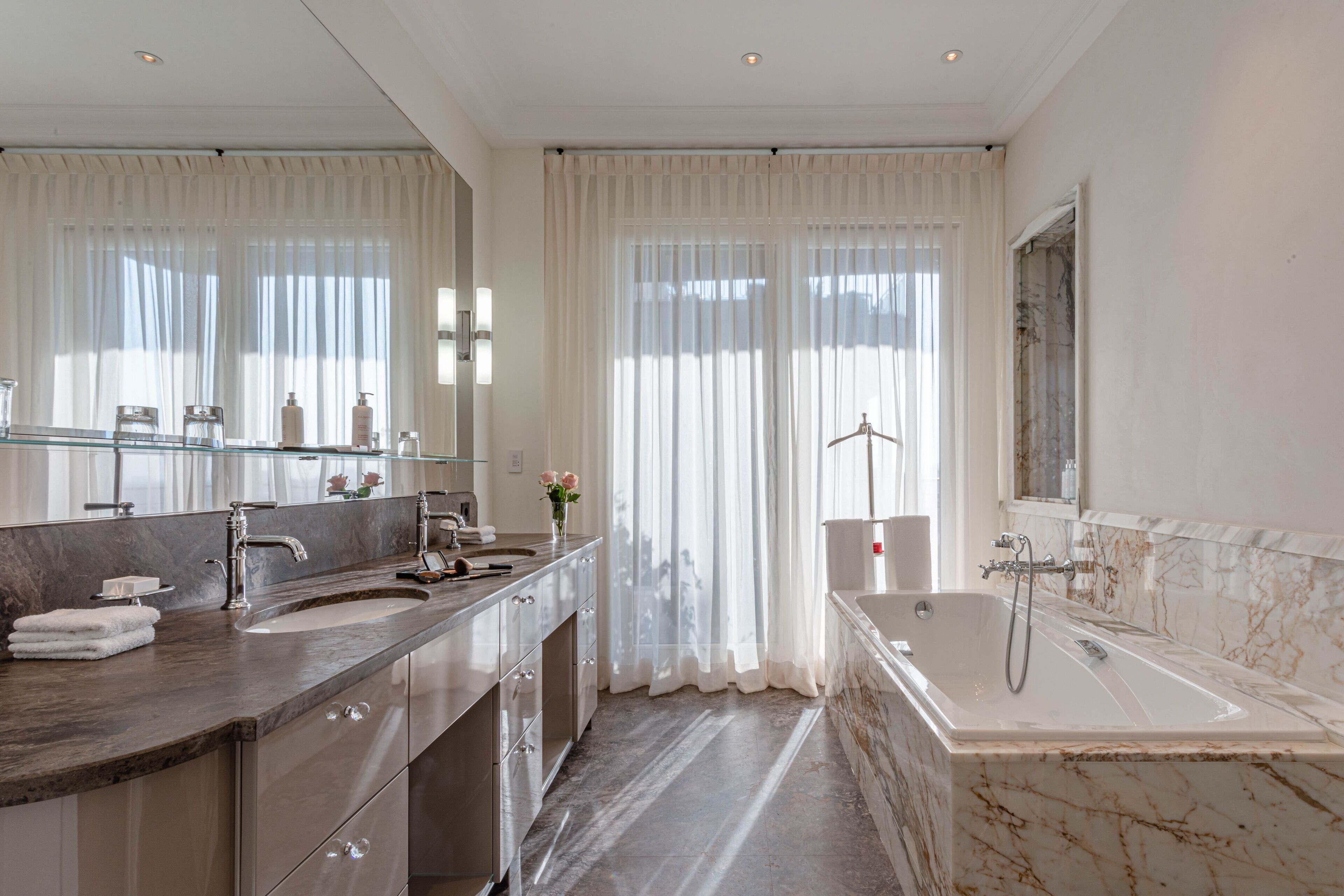 Un baño moderno con lavamanos de mármol, bañera y un espejo grande.