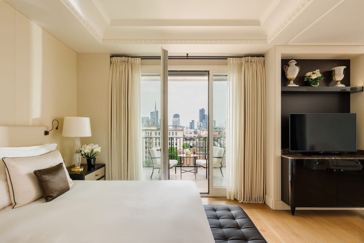 Ein Hotelzimmer mit einem großen Bett, einem Fernseher, einem Balkon mit Stadtblick und einem kleinen Tisch mit Blumen.