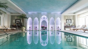 An indoor swimming pool with clear water, lounge chairs, and a decorative archway with framed pictures. - Palazzo Parigi Hotel & Grand Spa Milan (Milan)