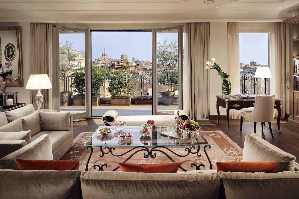 Ein geräumiges Wohnzimmer mit einem Glastisch, beigen Sofas und Blick auf eine Stadtlandschaft durch große Fenster.