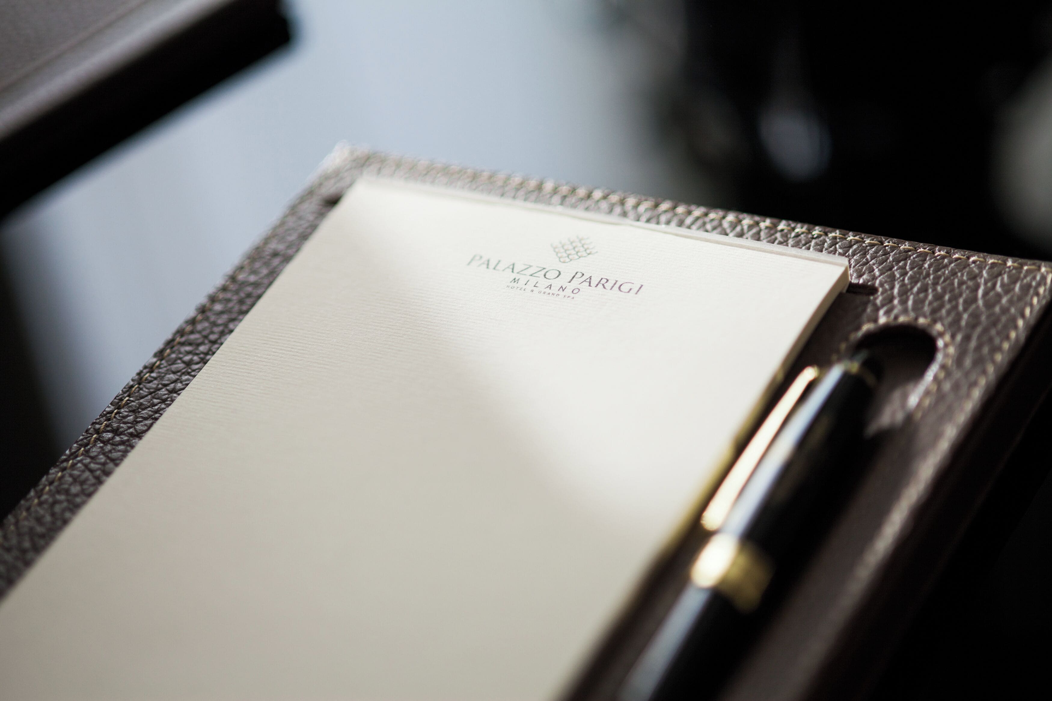 A notebook with 'PALAZZO PARIGI MILANO' text, a pen, and a textured notebook cover.