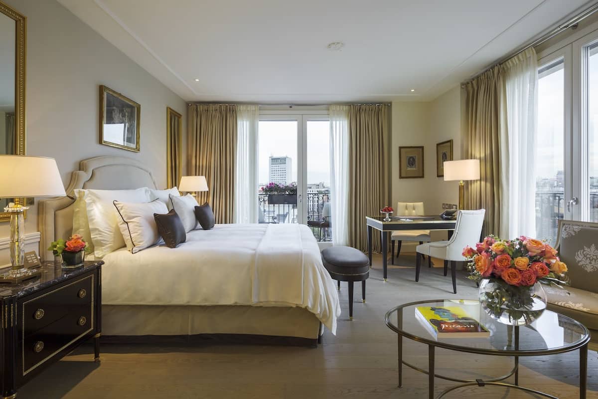 Ein Hotelzimmer mit einem großen Bett, einem Schreibtisch, einem Stuhl, einer Couch, einem Glastisch und Blick auf die Stadt.