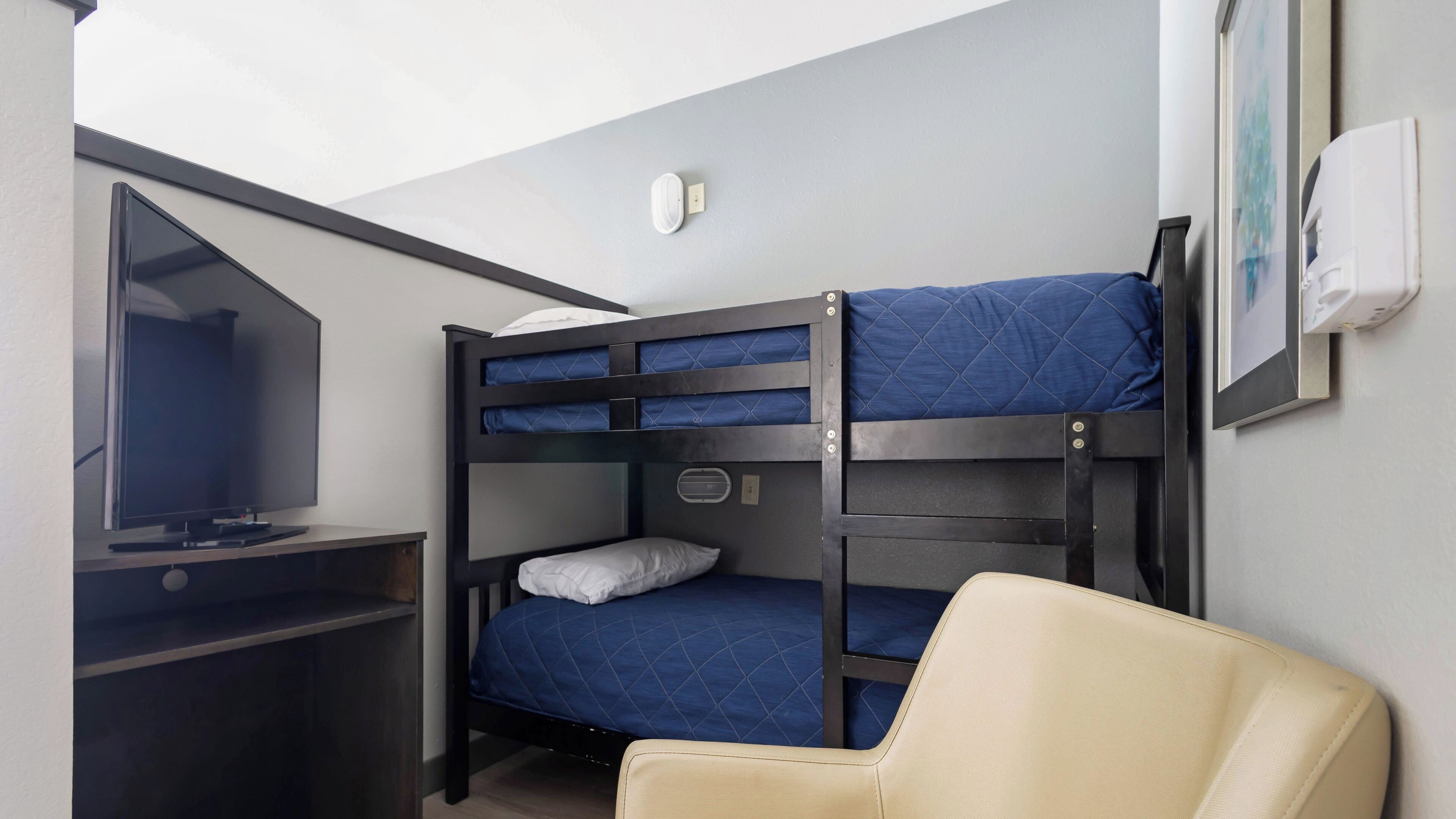 A bunk bed room with a television on a desk, a chair, and a wall-mounted air conditioner.