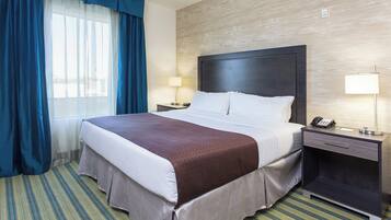 Habitación de hotel con una cama grande, una mesita de noche con teléfono, una lámpara y una ventana con cortinas azules.