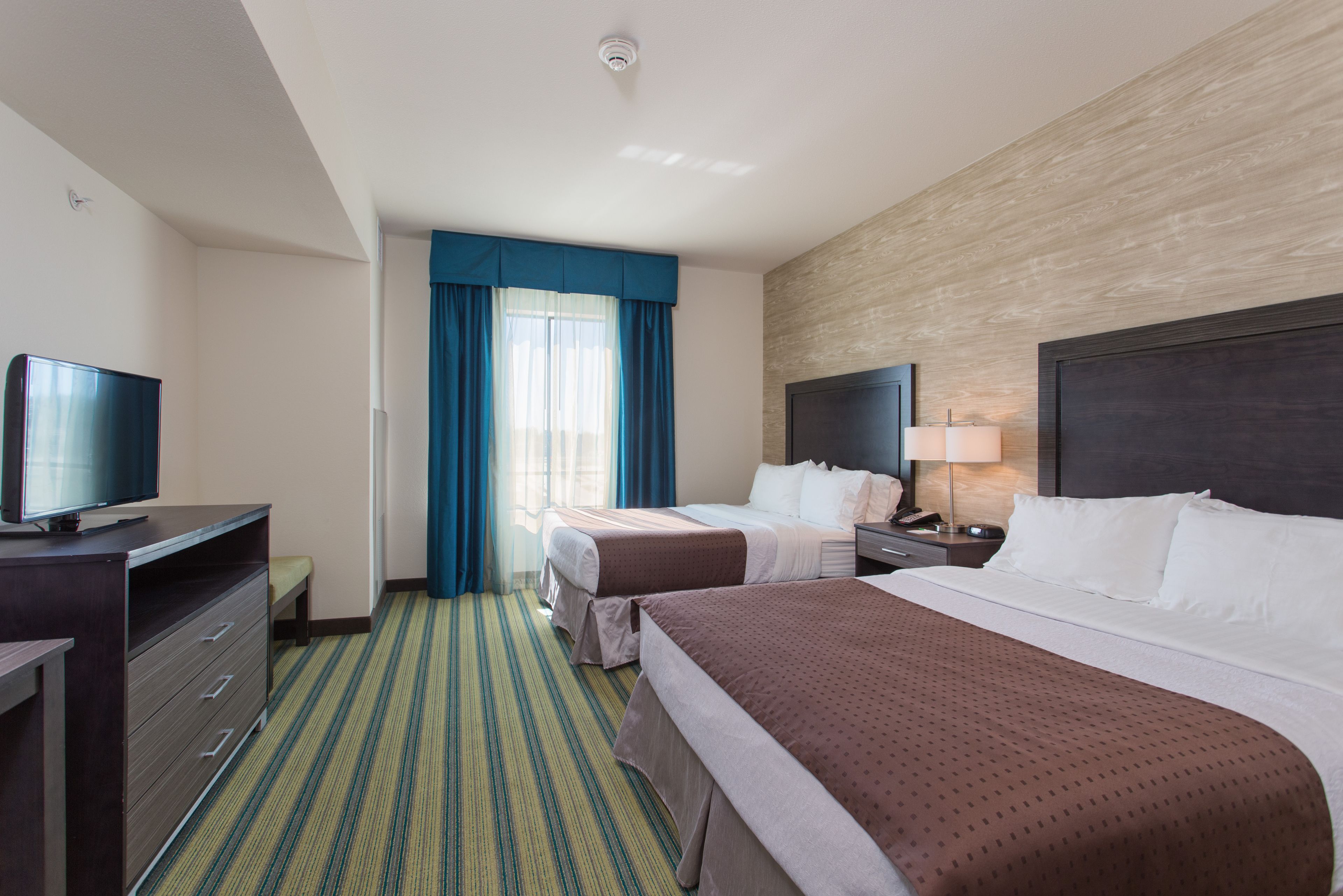 Une chambre d’hôtel avec deux lits, une télévision, un bureau et une fenêtre avec des rideaux.
