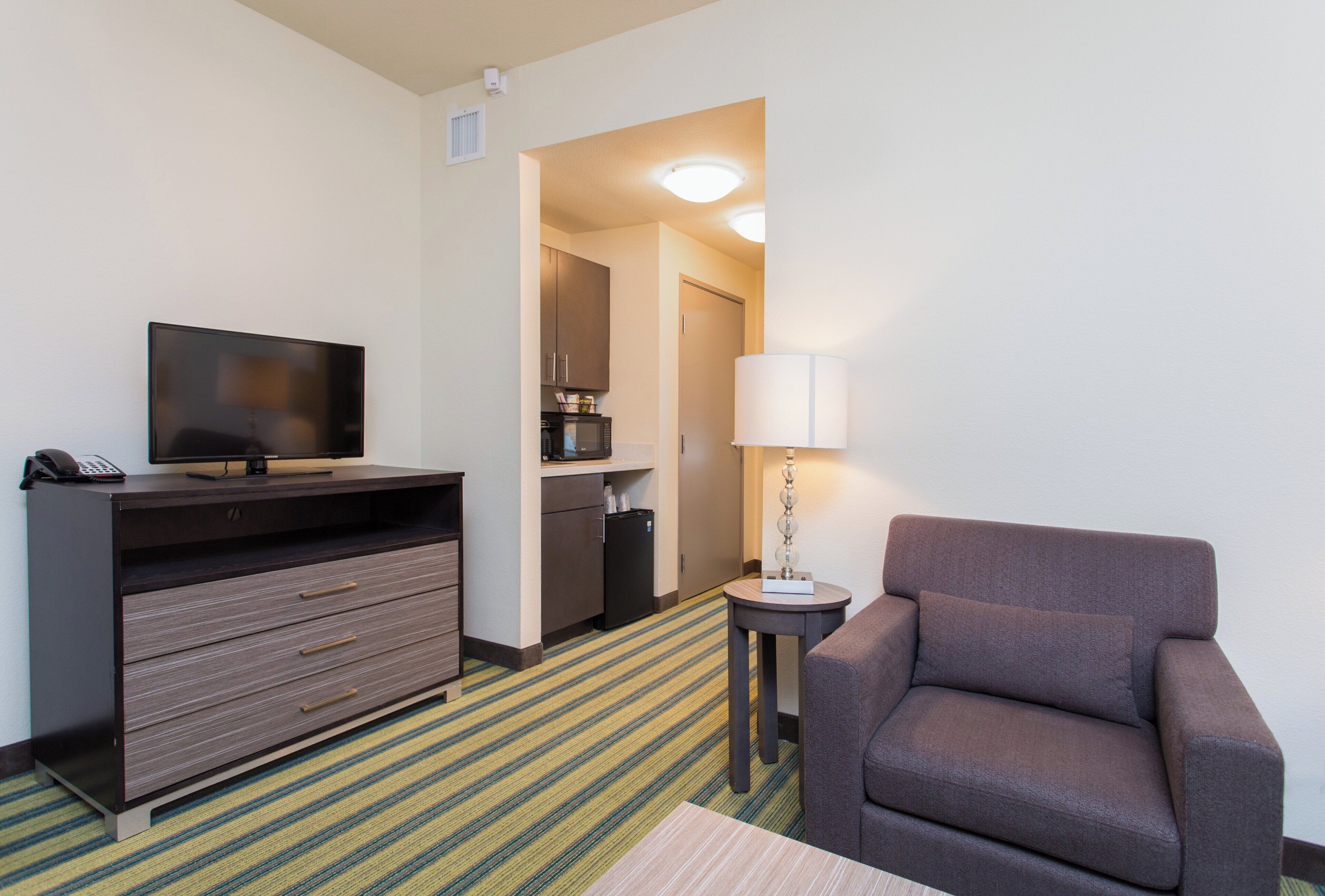 Une chambre d’hôtel équipée d’une télévision, d’un bureau avec des tiroirs, d’une chaise, d’une lampe et d’un four à micro-ondes.