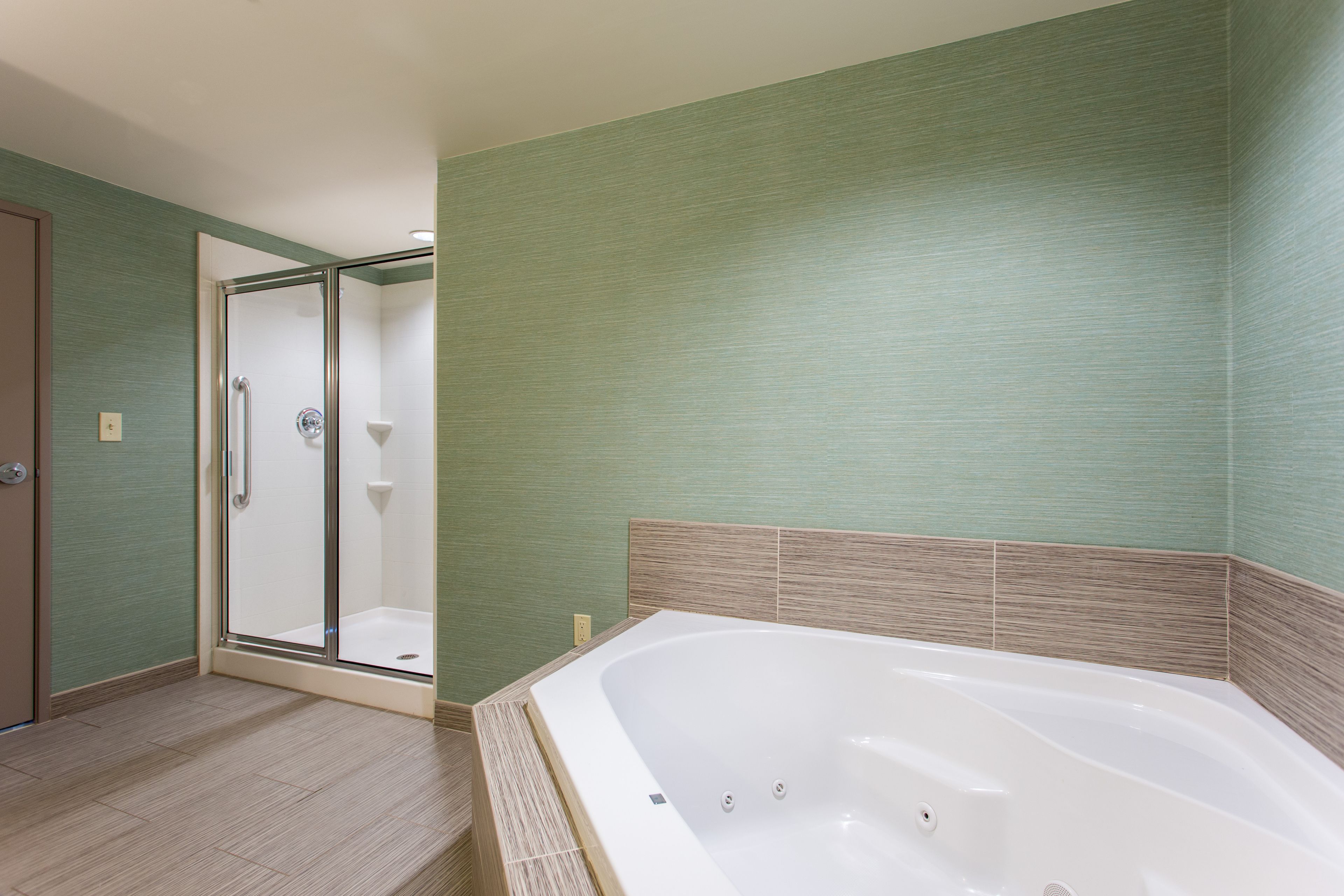 A bathroom with a glass shower enclosure, a bathtub, and a green-tiled wall.