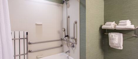 A bathroom with a white bathtub, grab bars, a towel rack with towels, and a shower head.
