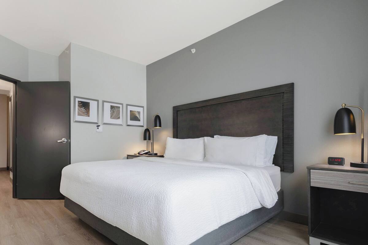 A modern hotel room with a large bed, bedside lamps, a nightstand, and framed artwork on the wall.