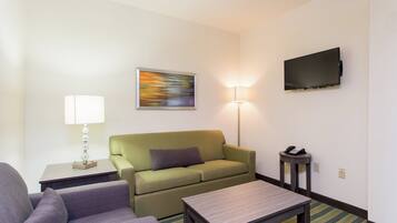 A hotel room with a green sofa, a small table, a lamp, a television, and a telephone on a side table.