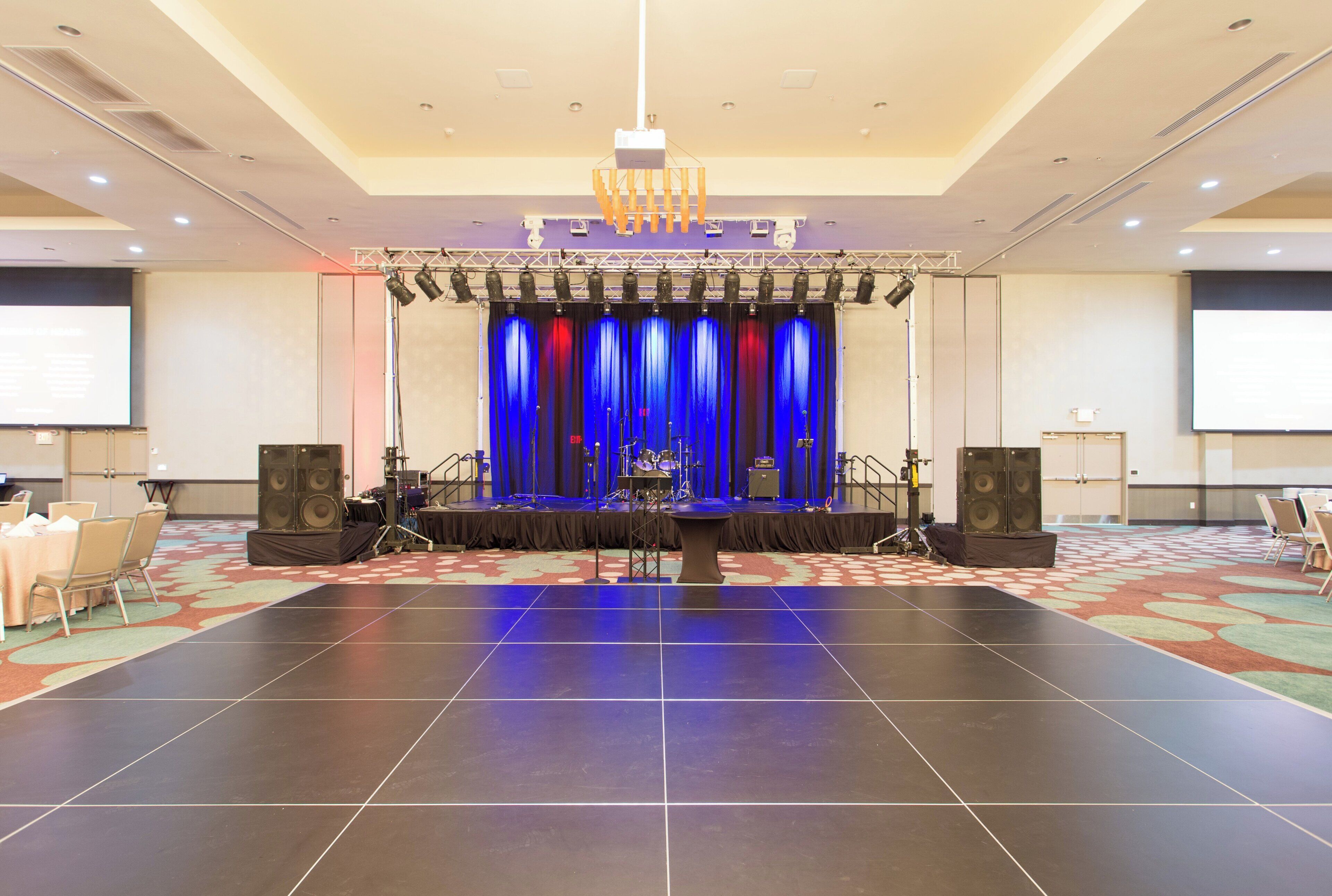 A conference room with a stage, large speakers, and a carpeted floor.