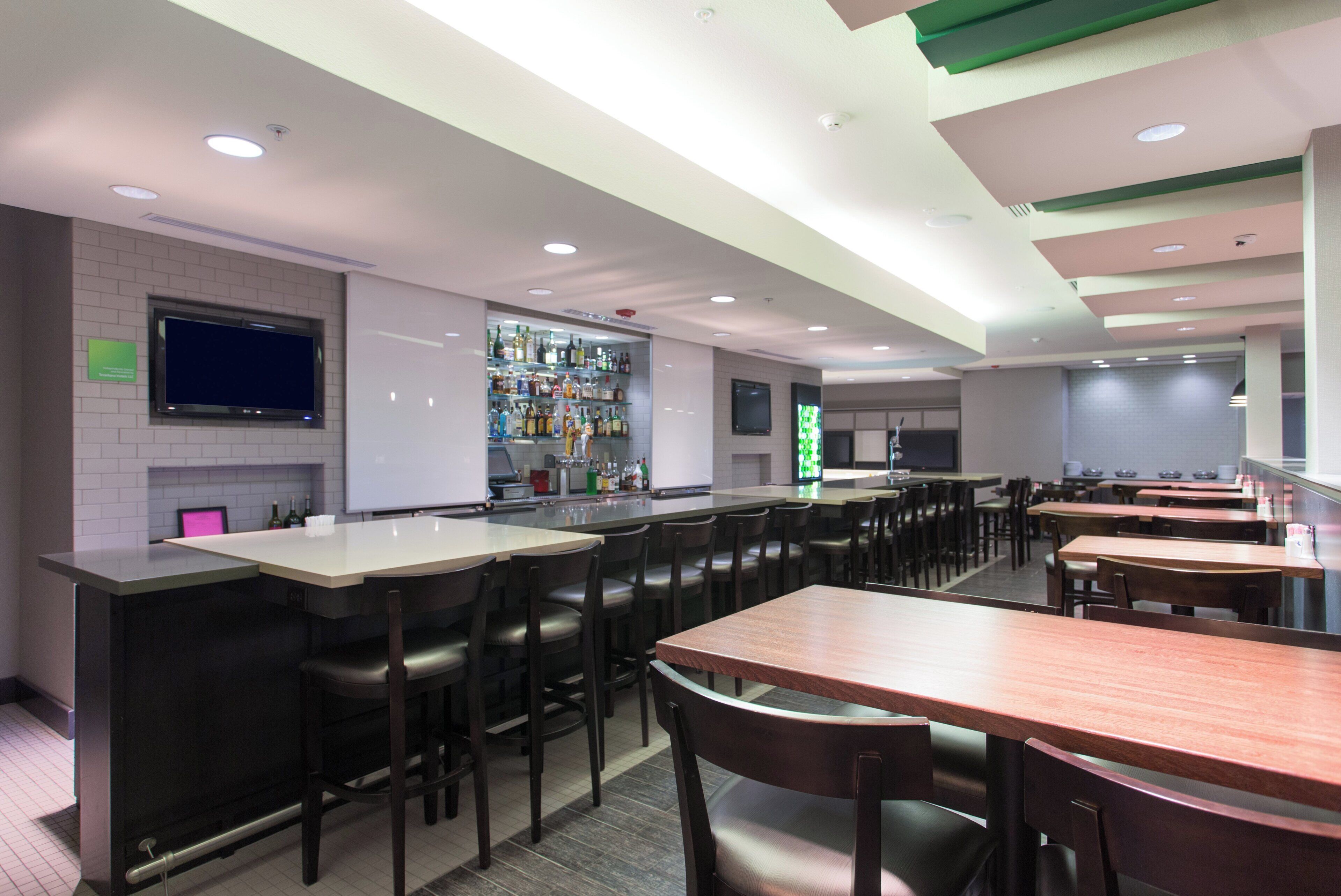 A modern restaurant with a bar area, multiple seating options, and a television screen mounted on the wall.