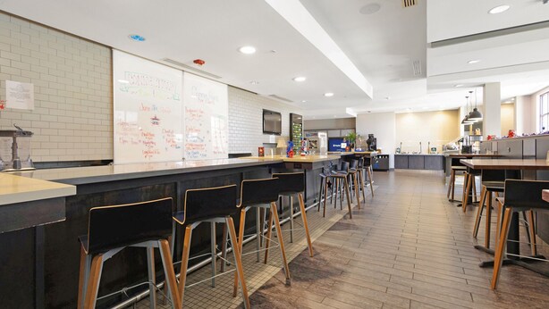 A modern kitchen area with a whiteboard, bar stools, and a long counter. - Holiday Inn Texarkana Arkansas Conv Ctr by IHG (Texarkana)