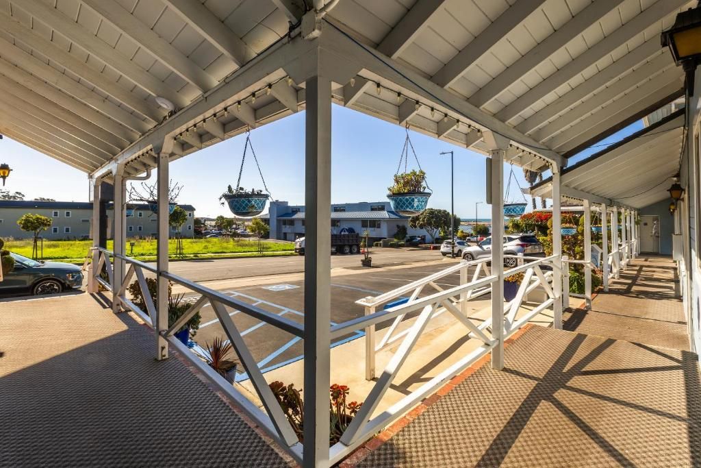 Un espacio exterior cubierto con estructura de metal, macetas colgantes y un estacionamiento al fondo.
