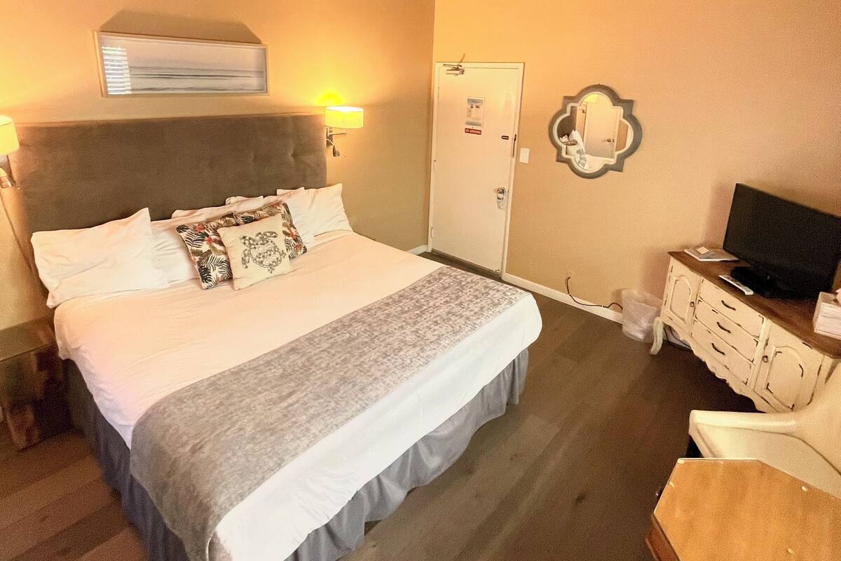A hotel room with a large bed, a television, a desk, and a wardrobe.