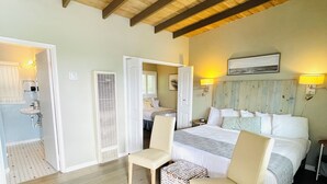 A hotel room with a wooden ceiling, a large bed, two chairs, a small table, and a bathroom visible through an open door. - Pleasant Inn (Morro Bay)