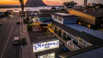 Un motel con un letrero, un estacionamiento y vistas al océano y una montaña al atardecer.