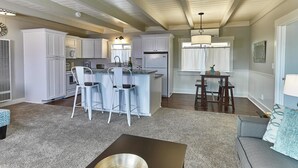 A spacious kitchen with white cabinets, a central island with bar stools, and a dining area with a table and chairs. - Pleasant Inn (Morro Bay)
