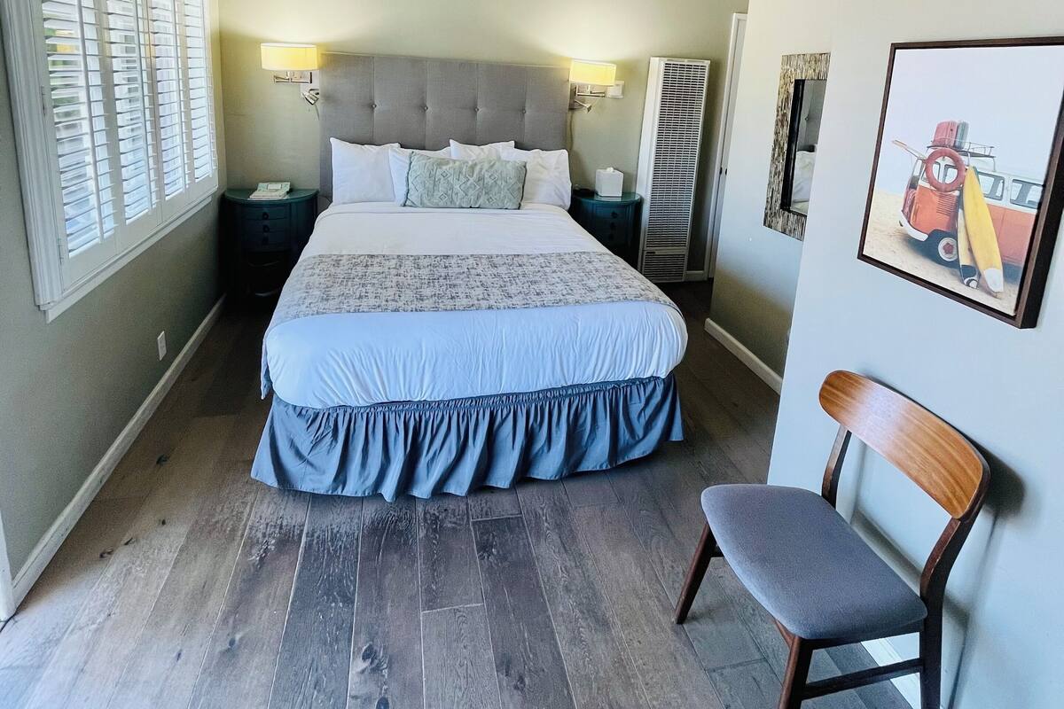 A bedroom with a bed, a chair, a nightstand, and a wall-mounted lamp.