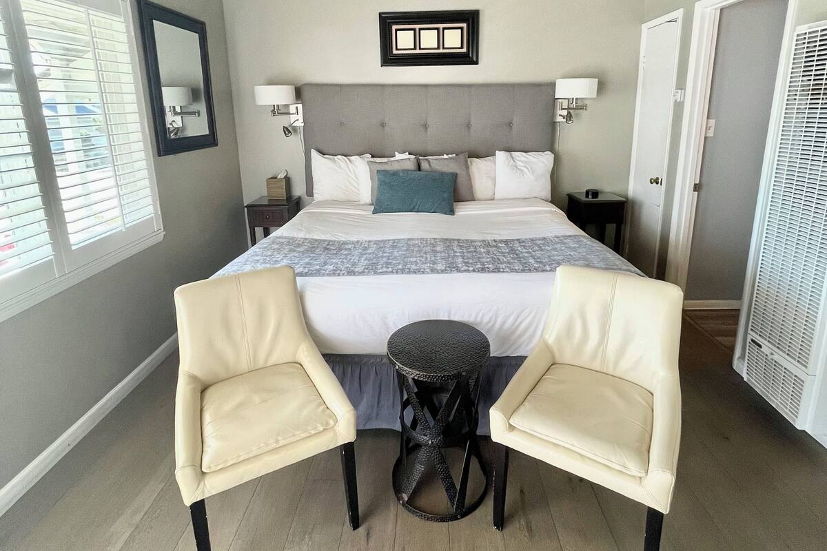 A bedroom with a large bed, two chairs, a small table, a nightstand, and a ceiling fan.