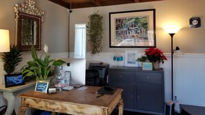 A cozy room with a wooden ceiling, a framed picture of a cafe, a desk with a computer, and a sign indicating a newsletter signup. - Pleasant Inn (Morro Bay)