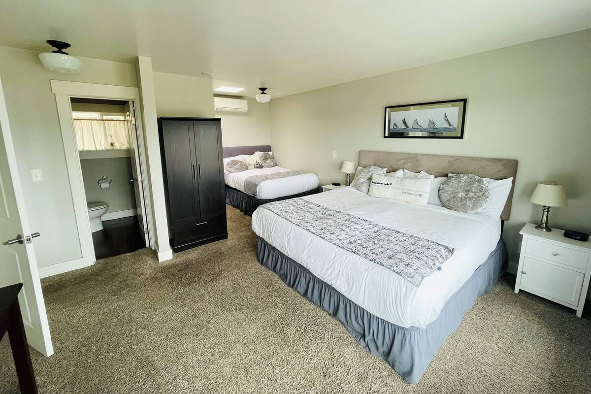 A hotel room with a large bed, a wardrobe, a bathroom, and a nightstand with a lamp.