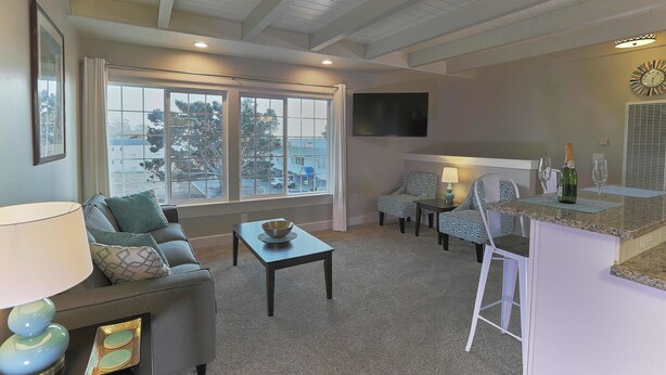 A living room with a sofa, a coffee table, a TV, and a bar area with a bottle and glasses. - Pleasant Inn (Morro Bay)