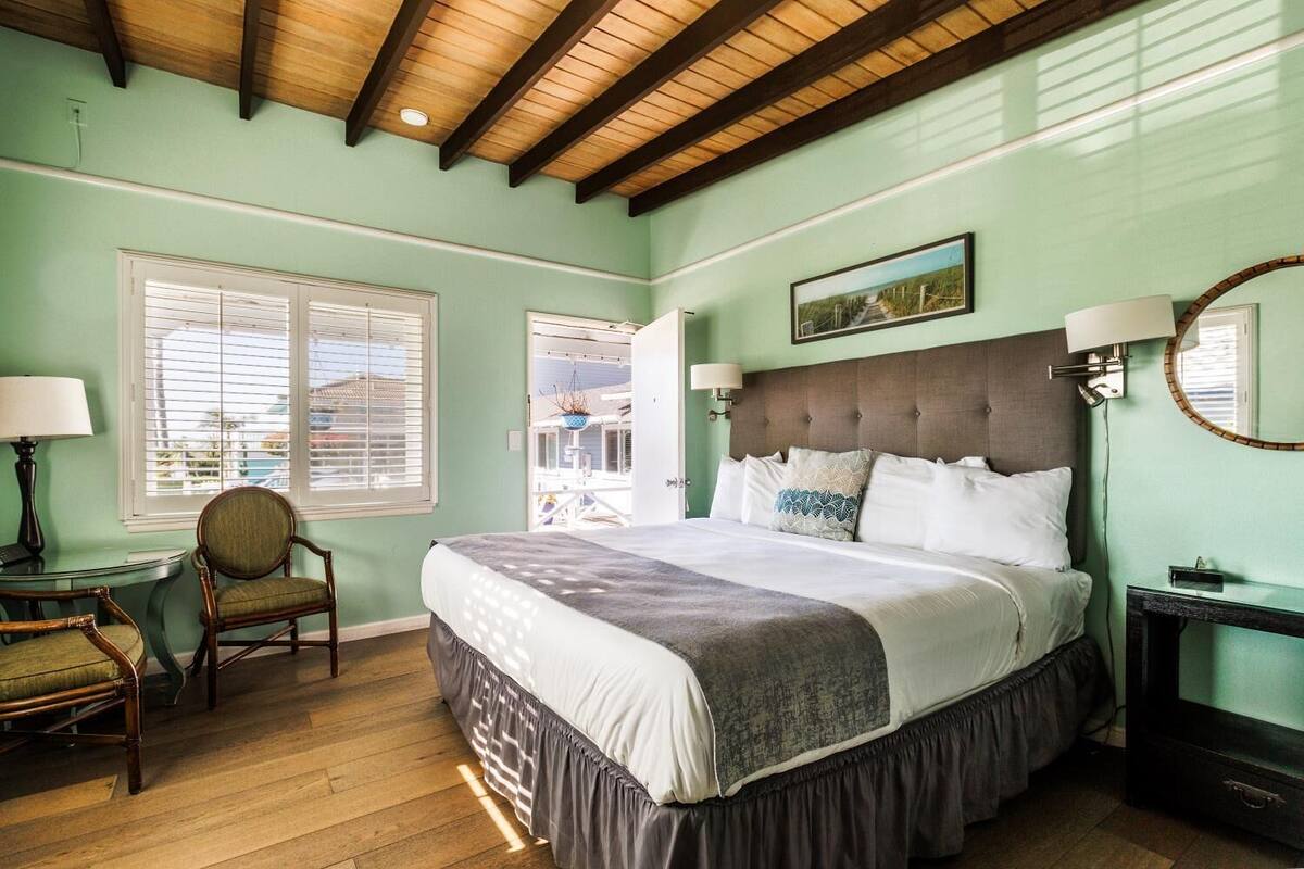 A bedroom with a large bed, a chair, a desk, and a window with blinds.