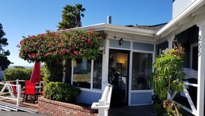 A covered patio area with a brick planter, a red chair, and a white table. - Pleasant Inn (Morro Bay)