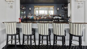 Een bar met streepstolletjes, een spiegel boven de bar, en planken vol flessen en glazen.