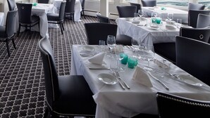 Een restaurant met gedekte tafels, grote ramen met uitzicht op de oceaan en een vloer met een patroon.