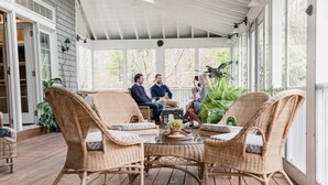 Een overdekt terras met rieten meubels en plantenpotten.