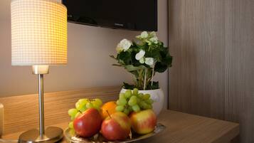 A wooden table with a fruit bowl containing apples and grapes, a potted plant with white flowers, and a lamp.