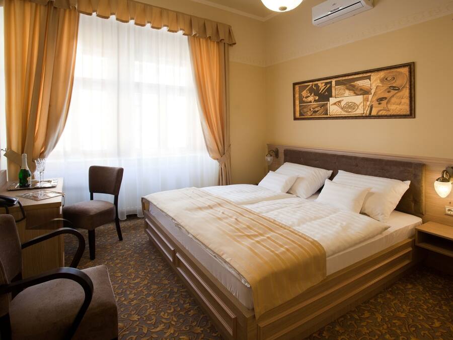 A hotel room with a large bed, a desk with a chair, a telephone, and a wall-mounted light fixture.