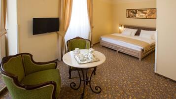 A hotel room with a bed, a TV, a green armchair, a table with teacups, and a patterned carpet.
