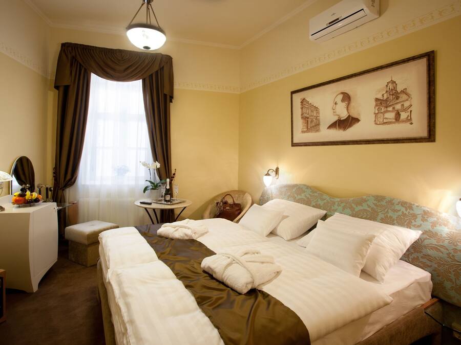 A hotel room with a large bed, a desk, a chair, a small table with a lamp, and a window with curtains.